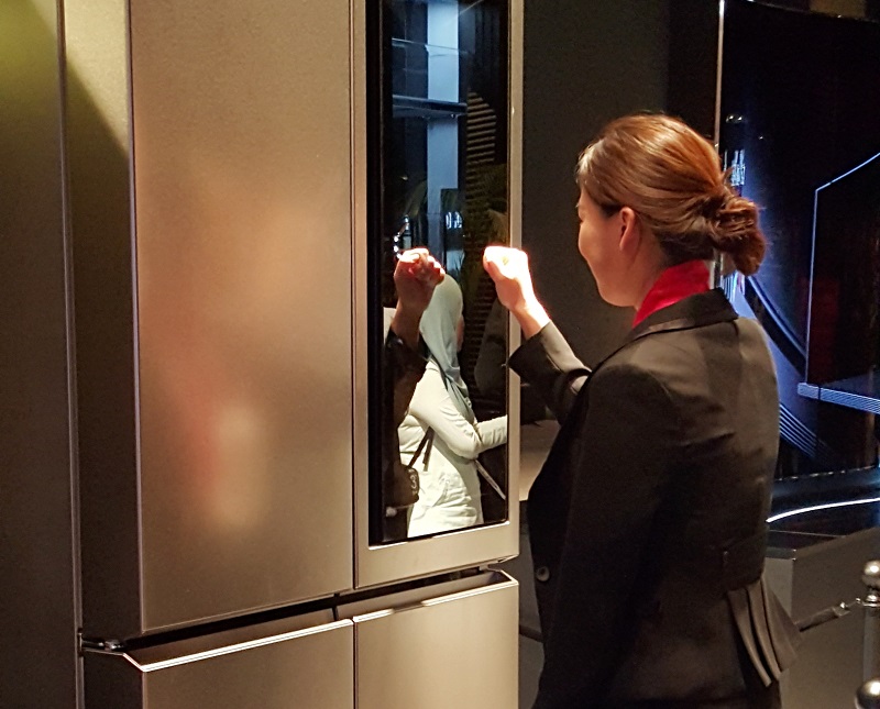 A staff member demonstrating how the opaque compartment of the refrigerator becomes transparent with a knock.