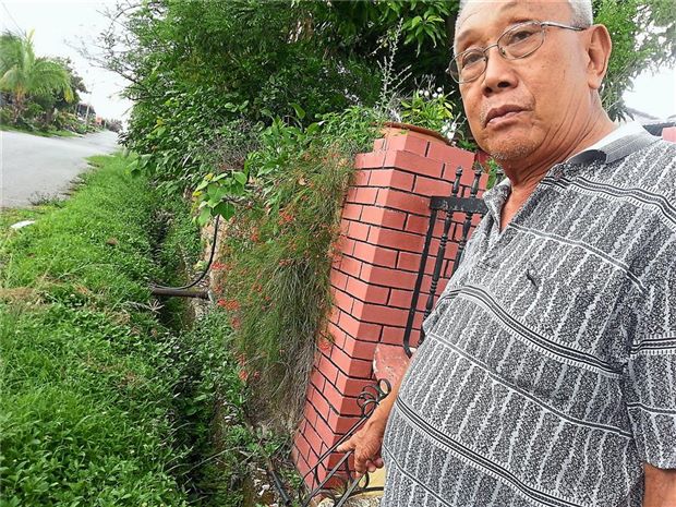 Weng showing a broken drain with overgrown plants at the village.