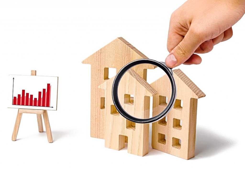 Magnifying glass is looking at the wooden houses with a stand of graphics and information. Growing demand for housing and real estate. Statistics on the state of the market. Investments.