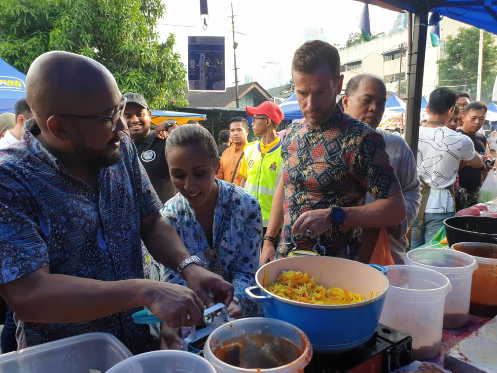 Syahrunizam Samsudin, CEO of TNG Digital Sdn Bhd, helping Yang Amat Mulia Tengku Datin Paduka Setia Zatashah binti Sultan Sharafuddin Idris Shah get food packed into tiffin carriers, with Dato' Setia Aubry Rahim Mennesson looking on.