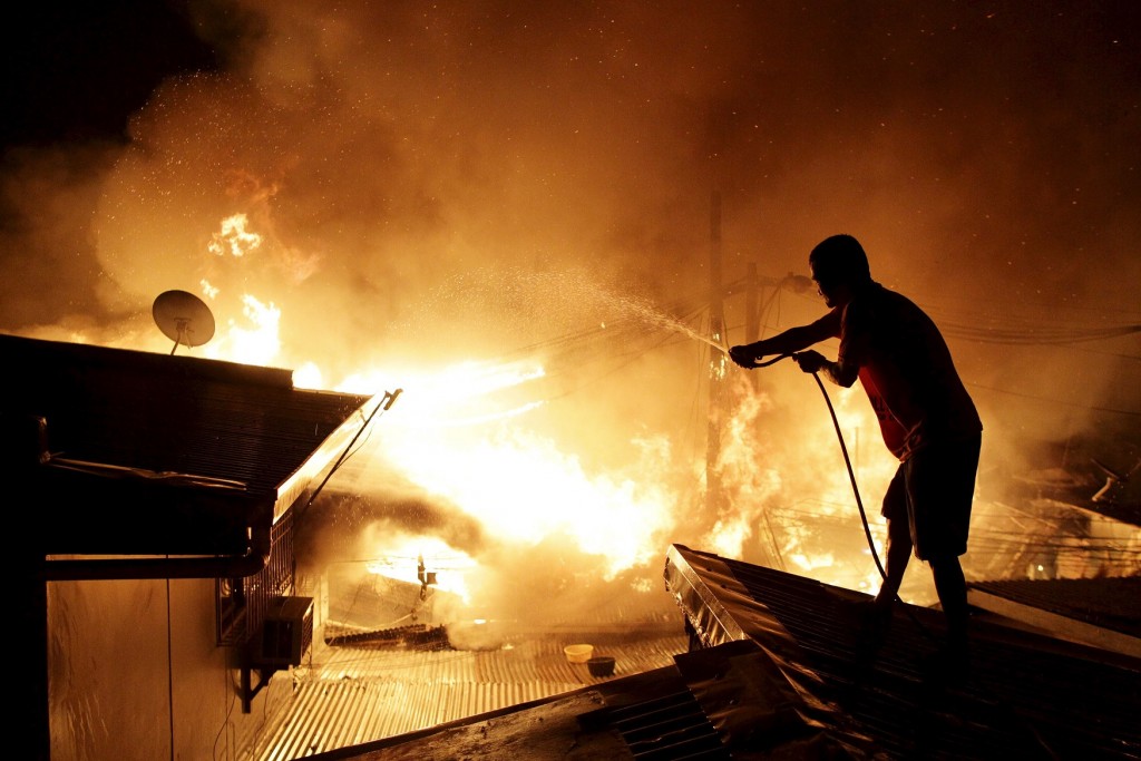 A resident uses a water hose on the roof of a house as he tries to extinguish a fire at a residential district in Manila