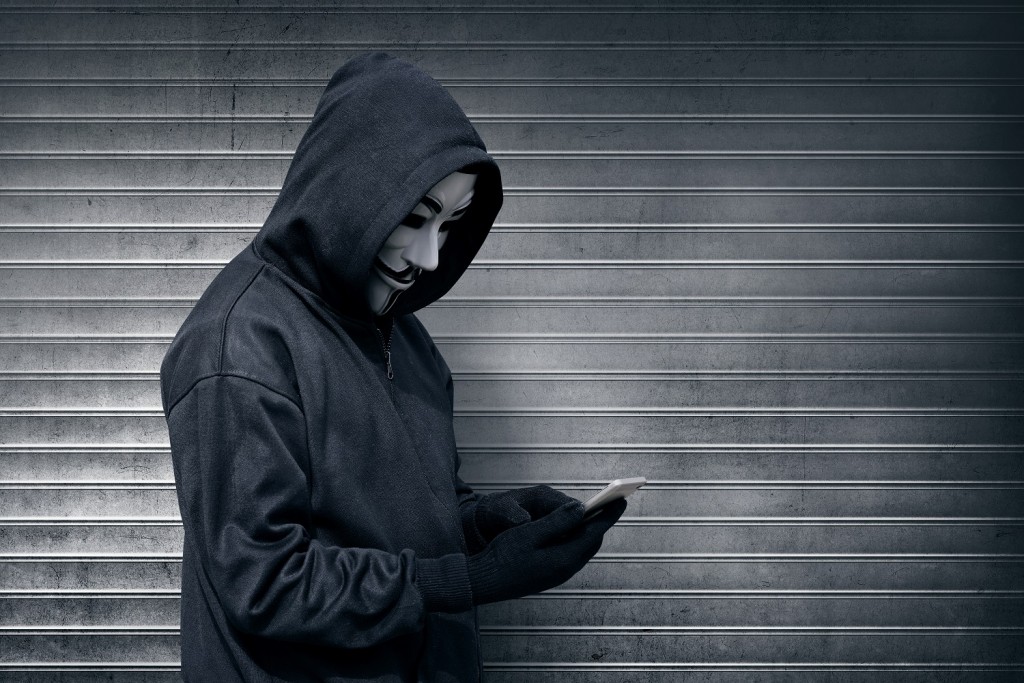 Hooded man with vendetta mask using mobile phone