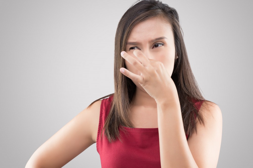 Asian woman in red shirt holding her nose because of a bad smell