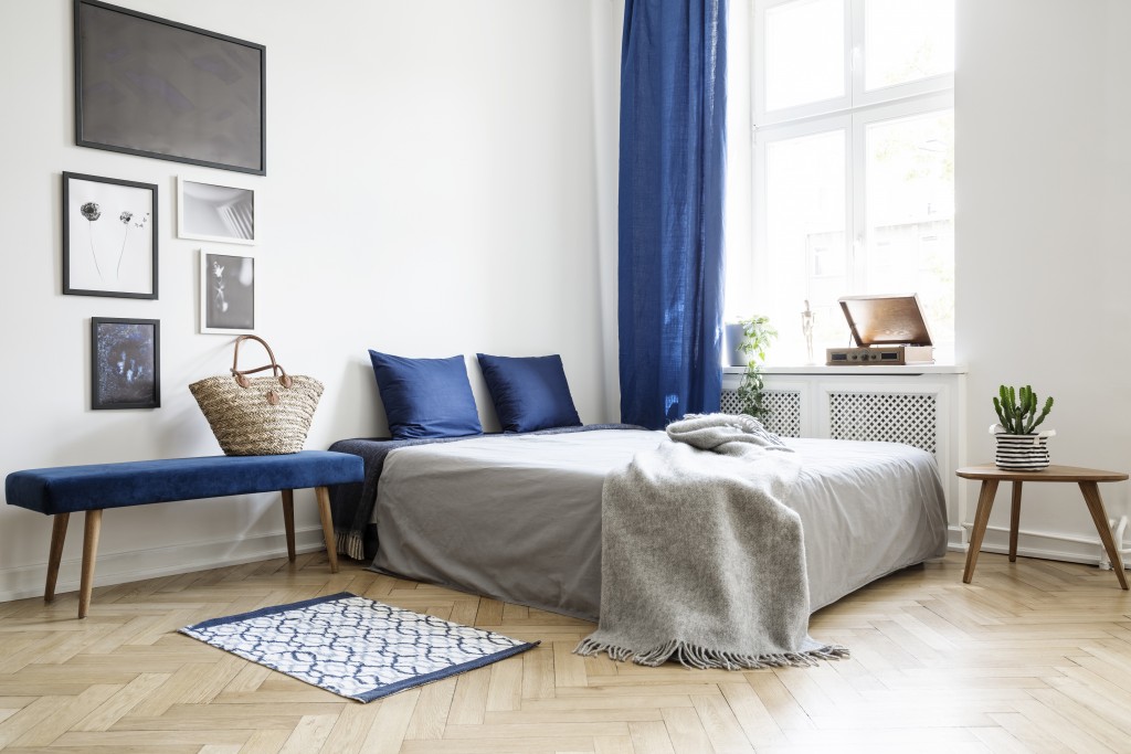 Bedroom design in modern apartment. Bed with dark blue pillows and grey duvet and blanket next to window. Real photo concept