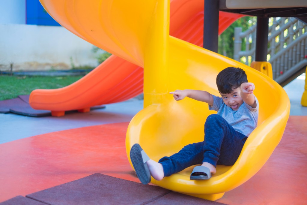 Asian kid playing slide at the playground under the sunlight in