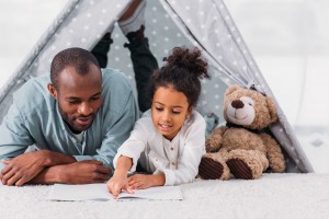 african american father and daughter reading book together at home