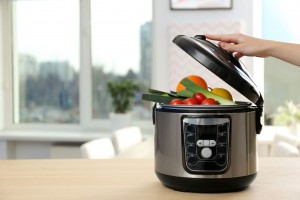 Young woman using modern multi cooker in kitchen, space for text