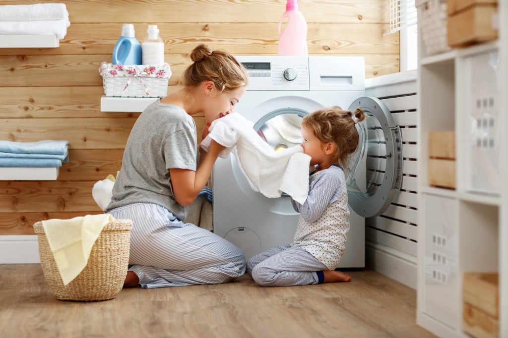 Happy family mother housewife and child in laundry with washing machine