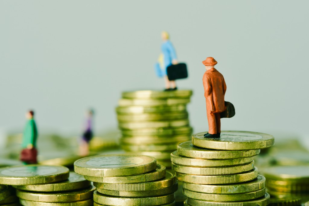 closeup of some miniature travelers carrying suitcases, on some piles of euro coins, with some blank space on the left